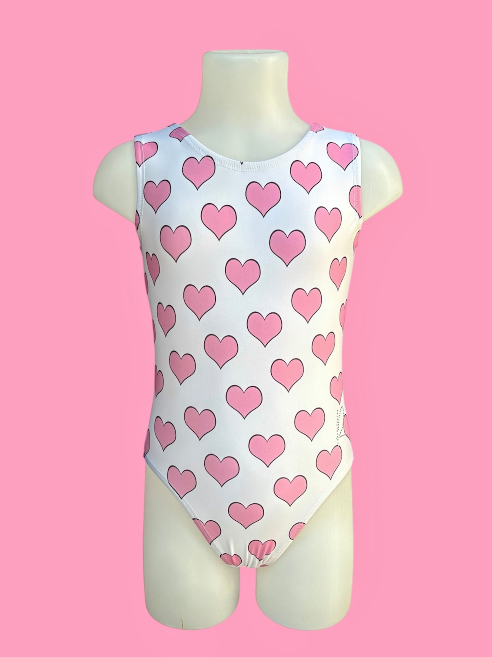 High-quality girls’ pink gymnastics leotard with heart print, sleeveless design, and professional stitching, ideal for toddlers and kids’ dance or gym practice in the UK. ‘R’ logo in small diamantés on left hip.